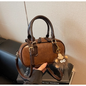 Close-up of vintage brown barrel bag with plush monster charm and leather strap details