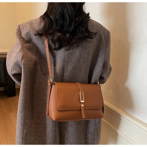 Brown lychee leather shoulder bag with gold metal buckle on a grey wool coat back view