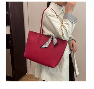 Detail of red lychee grain leather tote bag with floral silk scarf accessory on handle