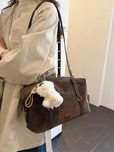 Large brown suede shoulder bag with plush pendant on casual beige trench coat