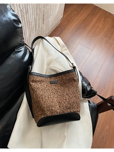 Detailed view of leopard print bucket bag with black leather trim and metal logo plate