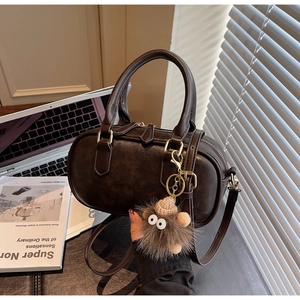 Close-up of retro brown leather boston bag with golden hardware and plush monster charm