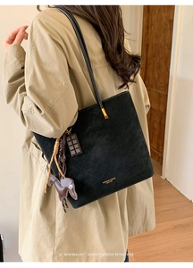 Detail of minimalist black matte tote bag with gold logo and cute puppy bag charm