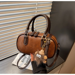 Detail of vintage brown Boston bag with smooth leather finish and cute plush monster charm
