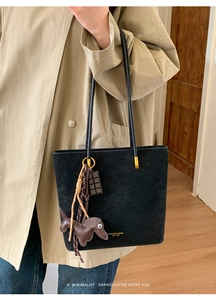 Close-up of black suede tote bag with cute dog charm and golden hardware detail