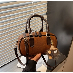 Close-up of brown suede Boston bag with golden hardware and cute hedgehog pendant