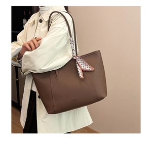 Detail of dark brown leather tote bag with silk scarf on handle worn by model