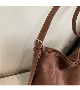 Detail of adjustable leather strap and silver metal buckle on brown suede tote bag
