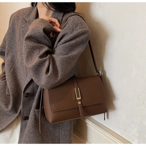 Detail of vintage brown pebble leather shoulder bag with sleek gold metal clasp on model