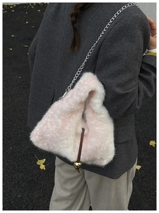 Detail of light pink plush chain bag featuring a golden ball pendant and silver metal strap