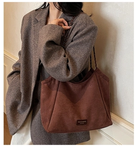 Détail du sac cabas en daim marron foncé avec bandoulière en chaîne et écusson en cuir