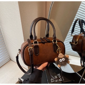 Detail of a brown Boston handbag with gold zippers and a plush doll charm accessory