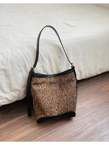 Detailed close-up of a leopard print bucket bag with black leather straps on wood floor