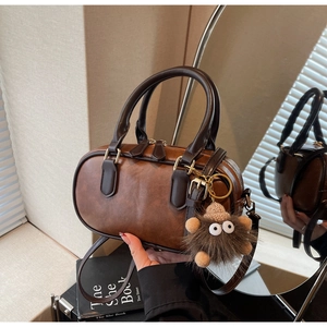 Detail view of brown leather Boston bag with plush monster charm and adjustable strap