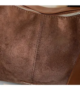 Détail du sac bandoulière en daim marron avec étiquette métallique et double couture