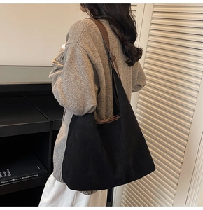 Detail of a large matte black tote bag with brown leather straps worn on shoulder