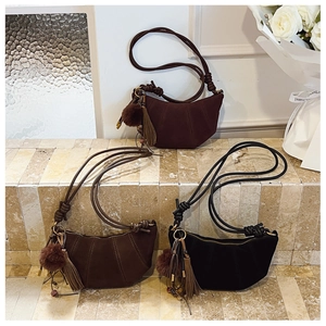 Detailed view of suede dumpling bags in various colors with tassels on stone steps