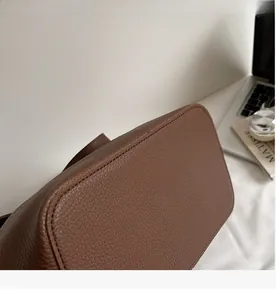 Gros plan du cuir grainé marron et des coutures précises sur le fond du sac à bandoulière