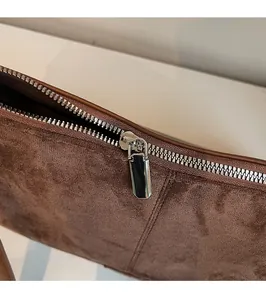 Détail de la fermeture éclair en métal argenté sur un sac bandoulière en daim marron