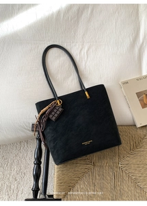 Close-up of black matte leather tote with gold logo and chocolate pendant on a rattan chair