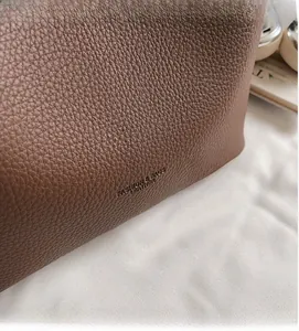 Gros plan sur la texture du cuir grainé marron et logo embossé sur le sac bandoulière chic