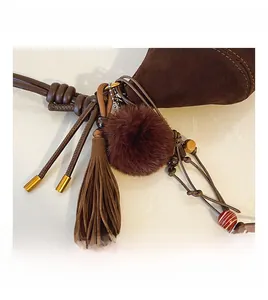 Detailed close-up of dark brown suede bag charms with tassels, fur pompom and beads