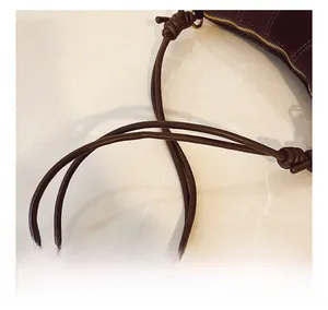 Detail of slim dark brown matte leather shoulder strap with a knotted design and gold zipper