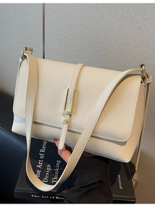 Vintage beige lychee pattern leather shoulder bag with gold buckle on black book prop