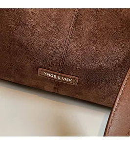 Gros plan d'un sac à bandoulière en daim avec logo métallique et coutures de précision