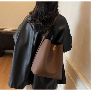 Sac seau marron en cuir grainé avec fermoir doré porté par un mannequin chic