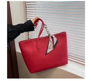 Detail of red pebbled leather tote bag with floral scarf handle and spacious design