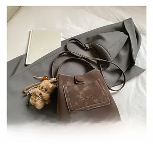 Detail of brown suede handbag featuring embossed logo and cute plush dog pendant