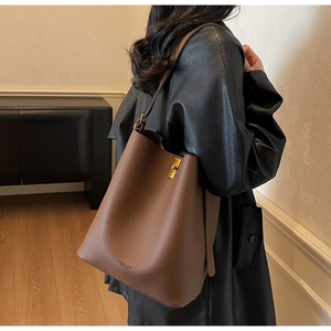Sac seau en cuir grainé marron porté par un modèle avec des boucles dorées
