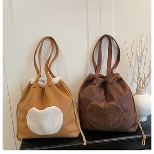 Detail view of plush drawstring bucket bags in tan and dark brown with heart patches