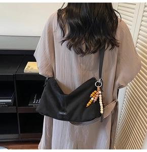 Détail d'un sac demi-lune noir avec un gland en perles décoratives et plaque de logo