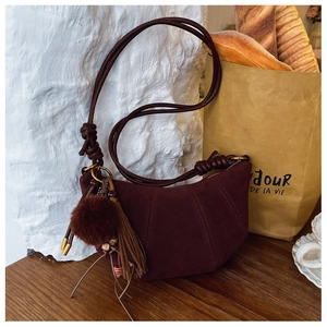 Detail of burgundy suede croissant bag with tassel and plush ball on a wooden table