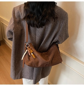 Détail du sac demi-lune en daim marron avec gland en perles de bois et logo