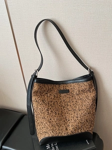 Leopard print bucket bag with black leather trim displayed on a modern bench