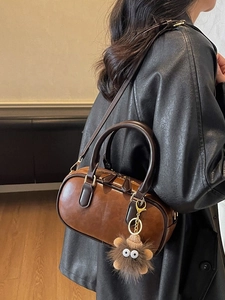 Coffee brown Boston barrel bag with plush charm and gold hardware on model