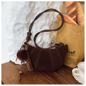 Close-up of matte suede crescent bag with fringe tassel and plush ball ornaments