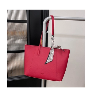 Close-up of red pebbled leather tote bag with floral scarf and embossed logo detail