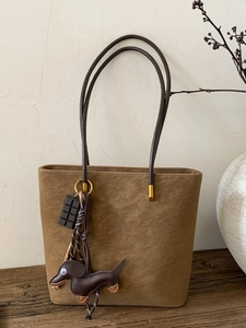 Minimalist brown suede tote bag with slim dark straps and cute charms on a wooden surface