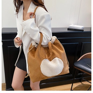Detail of a brown suede bucket bag featuring a large white plush heart and fuzzy trim