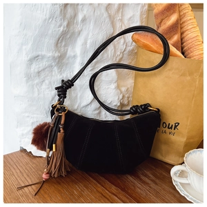 Close-up of black suede crescent bag with tassels, fur pompom and knotted strap detail