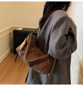 Sac hobo en daim marron avec pendentif à perles décoratif, porté à l'épaule par un mannequin