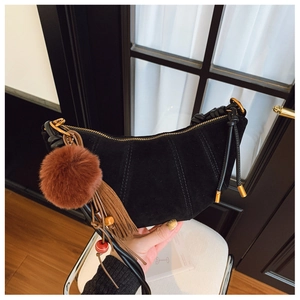 Macro view of black suede crescent bag featuring brown fur pompom and gold hardware detail