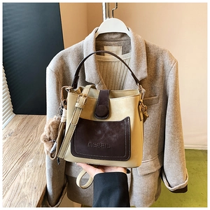Detail of two-tone bucket bag with MERFIL logo, top handle, and brown pom-pom charm