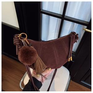 Detail of dark brown suede crescent bag with plush pom-pom and leather tassels