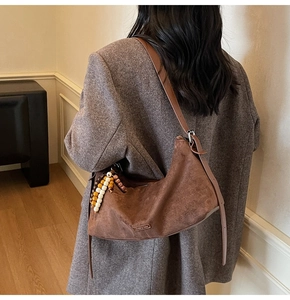 Détail du sac hobo en daim marron avec breloque en bois et bandoulière en cuir réglable