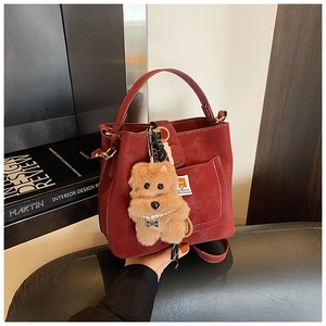 Detail view of burgundy matte bucket bag with stitching and plush charm decoration